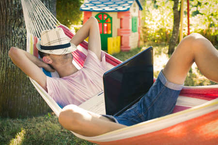 young man or teenager with the laptop in the hammock at sunset summerの写真素材