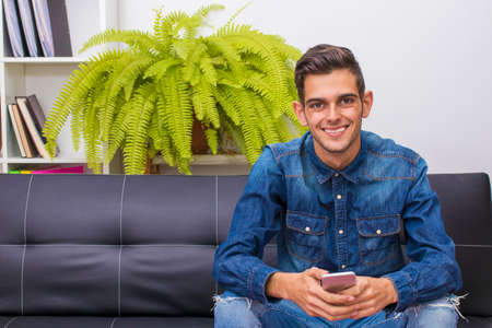 young man sitting on the couch with the mobile phoneの写真素材