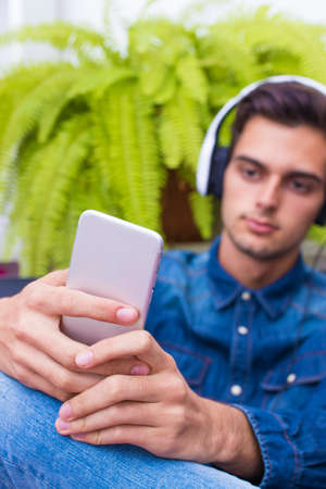 young man listening to music in the home Lounge with phone and earphones