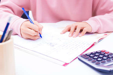 student hand writing with calculator at home or school