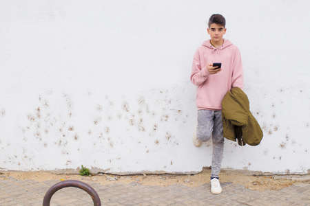 young teenager with mobile phone on the wall of the city streetの写真素材