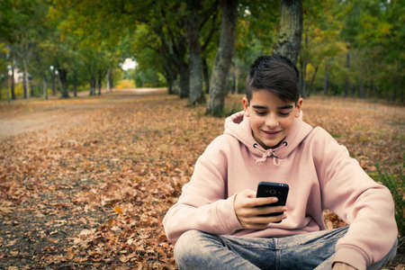 young teenager with mobile phone in the park in the fallの写真素材