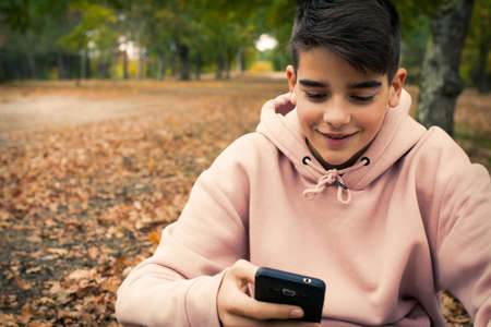 young teenager with mobile phone in the park in the fallの写真素材