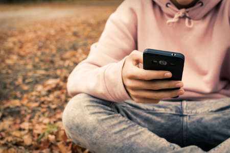 young teenager with mobile phone in the park in the fallの写真素材