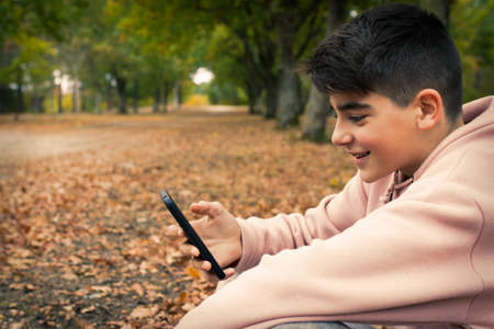 young teenager with mobile phone in the park in the fallの写真素材
