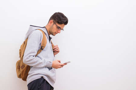 young man with mobile phone and backpack on the white wallの写真素材