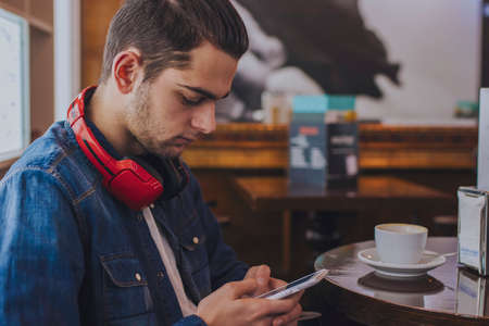 portrait of young with earphones and telephone in the cafeteriaの写真素材