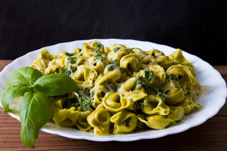 italian pasta dish prepared with cheese, vegetables and basil leafの写真素材