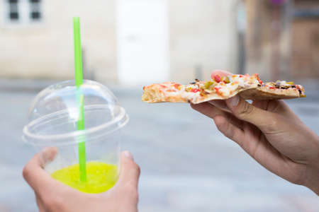 hand with portion of pizza and soda, eating in the streetの写真素材