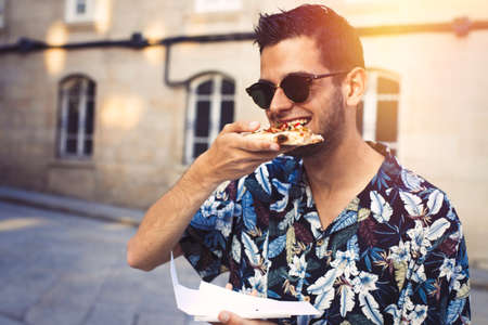 portrait of young man in the street of the city eating fast foodの写真素材