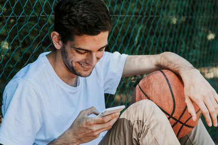 young smiley outdoor with mobile phone and basketballの写真素材