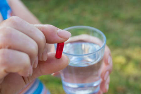 older woman hand with pills and a glass of waterの写真素材
