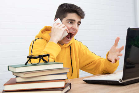 angry young man with mobile phone and laptop arguing or screamingの写真素材