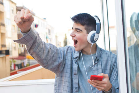 young euphoric with mobile phone and headphones celebrating successの写真素材
