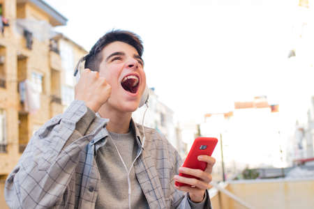 young euphoric with mobile phone and headphones celebrating successの写真素材