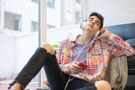 young man listening to music at home with headphones and phone
