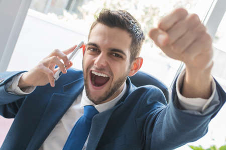 businessman triumphant with phone and celebrating successの写真素材