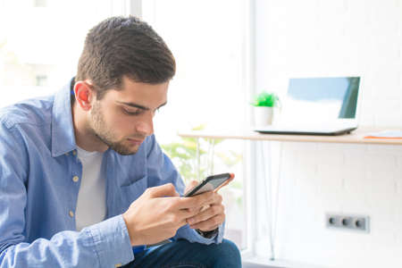 young man or teenager with mobile phone at home