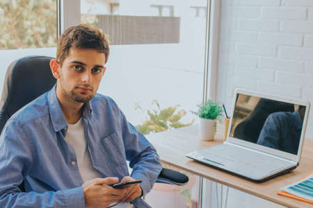 young man with mobile phone and laptop at homeの写真素材