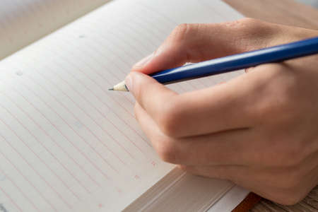 hand with the pencil writing in the book or notepad