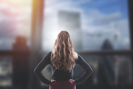 businesswoman in office building looking out the window at the skyscrapersの写真素材