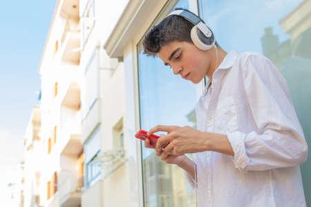 young man with phone and headphones listening to music outdoors in the city