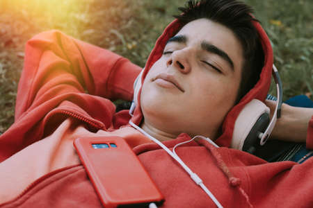 young teenage male with headphones and phone lying in the field