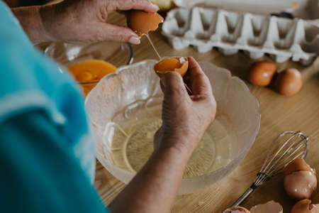 older woman's hands with eggs preparing cakes and sweets