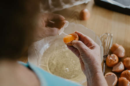 older woman's hands with eggs preparing cakes and sweetsの写真素材