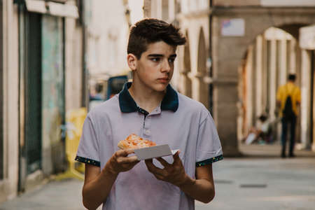 young man eating pizza by the city streetの写真素材