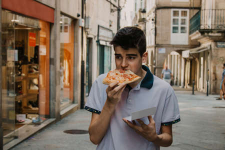 young man eating pizza by the city streetの写真素材
