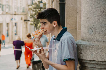 young man eating pizza by the city streetの写真素材
