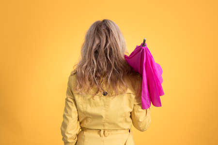 woman from behind with umbrella and raincoat isolated on color background