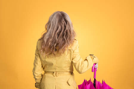 woman from behind with umbrella and raincoat isolated on color background