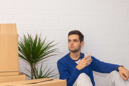 young man with moving boxes at home and mobile phone