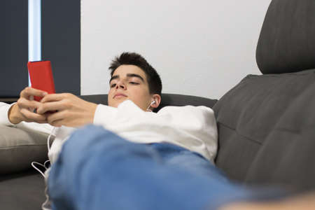 young teenage man with mobile phone on the sofaの写真素材