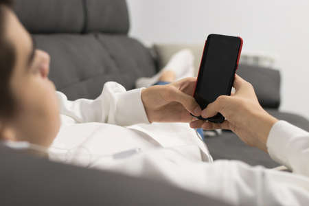 young teenage man with mobile phone on the sofaの写真素材
