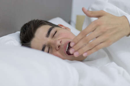portrait of young teenage man in bed sleeping with sleepy expressionの写真素材