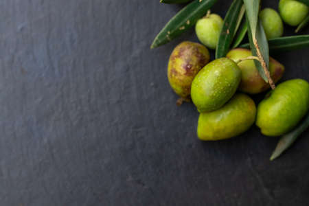 natural olives on black stone background with olive branches and spaceの写真素材