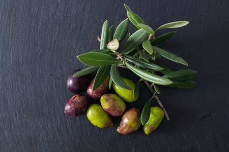 natural olives with olive leaves on black slateの写真素材