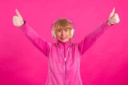 adult or senior woman with headphones and raised thumbs waving in approval or enthusiasm