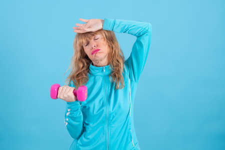 woman with expression of effort or tiredness with exercise dumbbells isolated on blue backgroundの写真素材