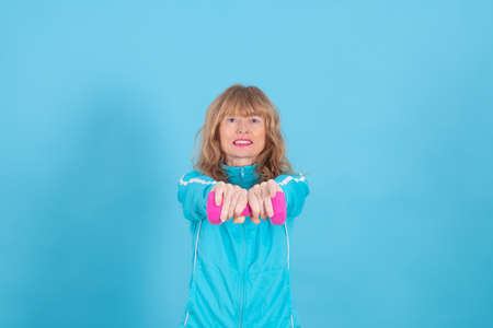 woman with expression of effort or tiredness with exercise dumbbells isolated on blue background