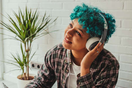 portrait of girl listening to music at home or apartment with mobile phone and headphonesの写真素材