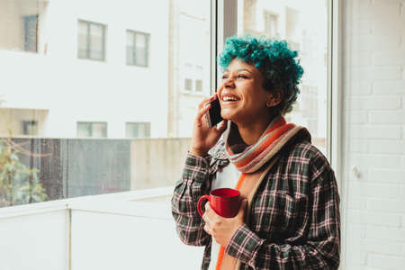 young girl talking on mobile phone at home or apartment with cupの写真素材