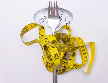 closeup of scale with measuring tape and fork, concept of diet and losing weight