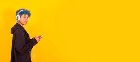 young girl with mobile phone and headphones isolated on color backgroundの写真素材