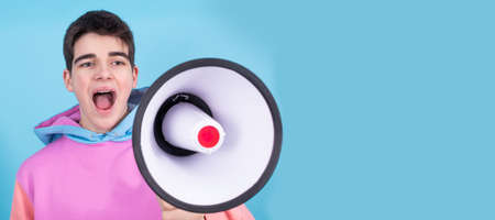 young teenage man or student with megaphone isolated on background with shout expressionの写真素材