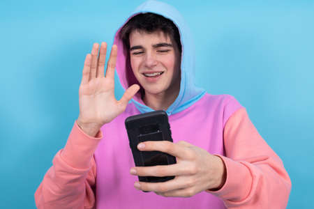 young teenager or student boy with hood and mobile phone isolated on color backgroundの写真素材
