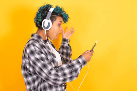 young brunette girl with mobile phone and headphones isolated on color backgroundの写真素材